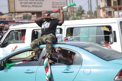  This supporter perched on a moving vehicle with a vuvuzela showing his excitement about his party's victory