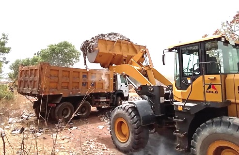 A pay loader evacuating refuse at a dump site into a truck