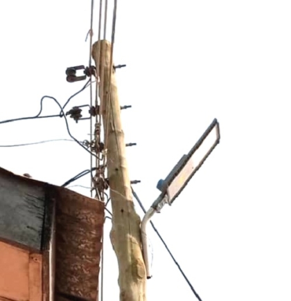 The weak electric pole with live wires on it leaning against the building 