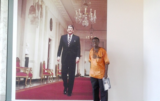 The writer standing in front of a portrait of Ronald Reagan, a former American President, at an Arts Gallery in Texas