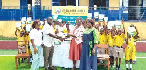 Godson Adzafi (2nd from left), Koforidua Area Manager of ASA Savings and Loans Limited, presenting one of the items to Gifty Edith Opoku (2nd from right), Eastern Regional Manager of Methodist Schools. Looking on are some of the teachers  and staff of the company while pupils display their exercise books