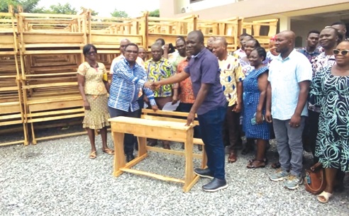  Simon Kweku Tetteh (right), Lower Manya Krobo NPP Parliamentary Candidate, handing over the furniture to Samuel Kwesi Tettey (left), GES Director of Education. Looking on are some of the teachers from the schools