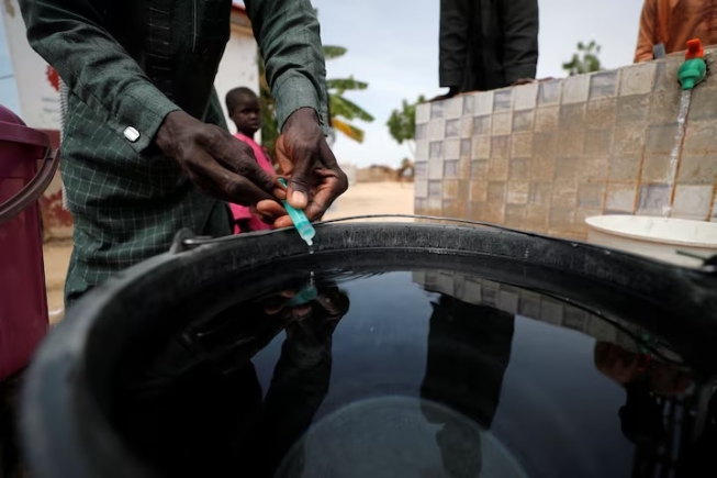 A community health worker adds chlorine to water while internally displaced people gather to fill their buckets at the water point in Muna Garage IDP camp in Maiduguri, Borno State, Nigeria October 23, 2022. REUTERS/Christophe Van Der Perre/File Photo