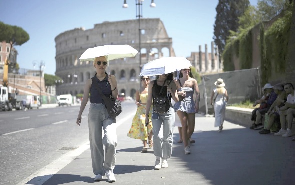 People using umbrellas in hot weather to shelter from the sun while walking past the Colosseum, in Rome
