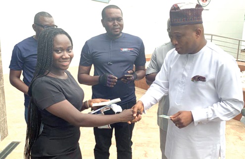 Doreen Klutse (left) in a handshake with Samuel Okudzeto Ablakwa (right), the Minister of Foreign Affairs, after receiving her passport at the Ghana Library Authority head office in Accra, as officials from Ghana Post look on