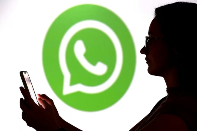 A teenager poses for a photo while holding a smartphone in front of a Whatsapp logo in this illustration taken September 11, 2025. REUTERS/Dado Ruvic/Illustration/File Photo