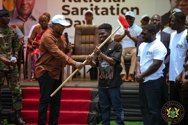 President John Mahama (left)  interacting with Heneba Kojo Sarfo (2nd from left), the leader of Bus Stop Boys, and other members after the presentation of a standing brush as part of the essential sanitation tools donation