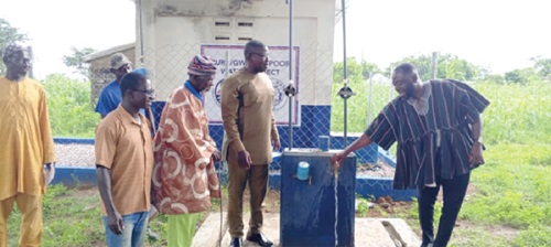 Seth Kponyo (right), PURC Regional Manager, opening the tap for water to flow from one of the boreholes, while Joseph Akaseje Abaa (2nd from right), Bongo DCE, and other guests look on