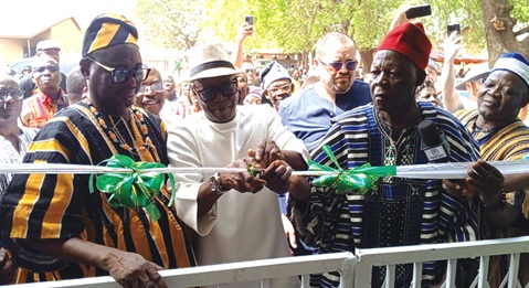 Donatus Akamugri Atanga (2nd from left), the Upper East Regional Minister, being supported by Naba Kosomo Legbe Serum-Tinganbila-Legbe Goo (left), Chief of Yorogo, and Roland Ayoo (right), MCE for Bolgatanga Municipality, to cut the tape while community members look on
