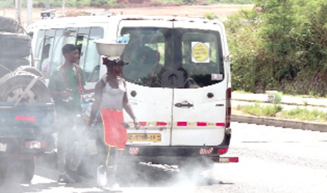 A bus emitting exhaust fumes, polluting the environment and posing a health hazard to street hawkers