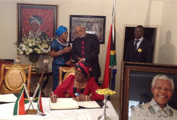 It is the turn of Mrs Rawlings to sign the book of condolence. In the background President Rawlings and SA High Commissioner, Ms Jeanette Ndhlovu discuss a point of interest.