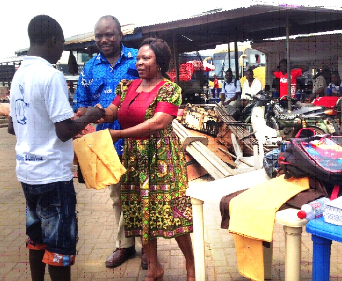 Madam Georgina Aberese-Ako of the Department of Children, Ministry of Gender, Children and Social Protection, being assisted by the Country Director of Afrikids Ghana, Mr Nicholas Kumah, to present a school uniform, exercise books and school bags to a beneficiary at a ceremony held at the main lorry park in Bolgatanga.